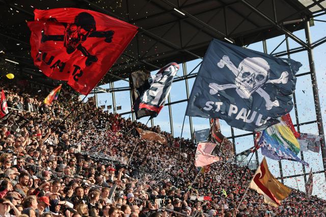 11 April 2026, Hamburg: St. Pauli fans waving flags in the stands during the German Bundesliga soccer match between FC St. Pauli and Bayern Munich at Millerntor Stadium. Photo: Christian Charisius/dpa - IMPORTANT NOTICE: DFL and DFB regulations prohibit any use of photographs as image sequences and/or quasi-video.