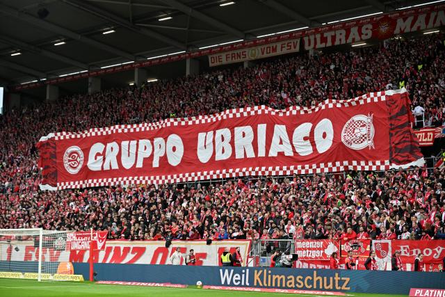 12 April 2026, Rhineland-Palatinate, Mainz: Mainz fans hold up a banner in the stands prior to the start of the German Bundesliga soccer match between FSV Mainz 05 and SC Freiburg at Mewa Arena. Photo: Torsten Silz/dpa - WICHTIGER HINWEIS: Gemäß den Vorgaben der DFL Deutsche Fußball Liga bzw. des DFB Deutscher Fußball-Bund ist es untersagt, in dem Stadion und/oder vom Spiel angefertigte Fotoaufnahmen in Form von Sequenzbildern und/oder videoähnlichen Fotostrecken zu verwerten bzw. verwerten zu lassen.