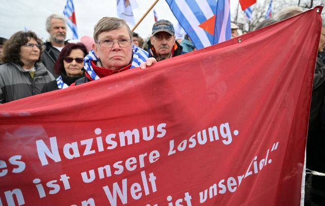 12 April 2026, Thuringia, Weimar: Vera Dehle-Thaelmann, the granddaughter of Ernst Thaelmann, the KPD chairman who was murdered at Buchenwald concentration camp, holds a banner during the 81st anniversary of the liberation of Buchenwald concentration camp. Photo: Martin Schutt/dpa