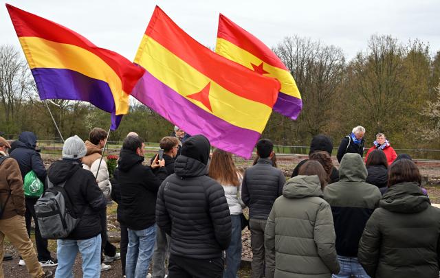12 April 2026, Thuringia, Weimar: Vera Dehle-Thaelmann, the granddaughter of Ernst Thaelmann, the KPD chairman who was murdered at Buchenwald concentration camp, speaks in front of the fluttering flags of the International Brigades during the 81st anniversary of the liberation of Buchenwald concentration camp. Photo: Martin Schutt/dpa