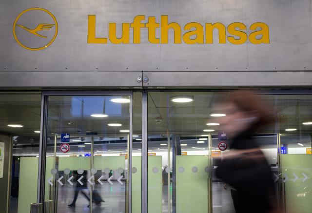 13 April 2026, Hesse, Frankfurt/Main: A woman walks in front of a Lufthansa sign at Frankfurt Airport. The Vereinigung Cockpit pilots' union has called for work stoppages at Lufthansa and several subsidiaries on Monday and Tuesday. Photo: Hannes P. Albert/dpa