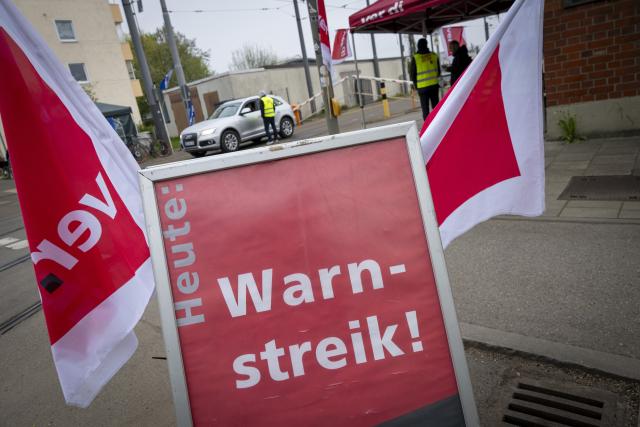 14 April 2026, Bavaria, Munich: Employees of the MVG East Depot stand behind a banner reading "Warning Strike Today" at the workshop gate on Truderinger Strasse during a warning strike affecting local public transportation. Photo: Peter Kneffel/dpa