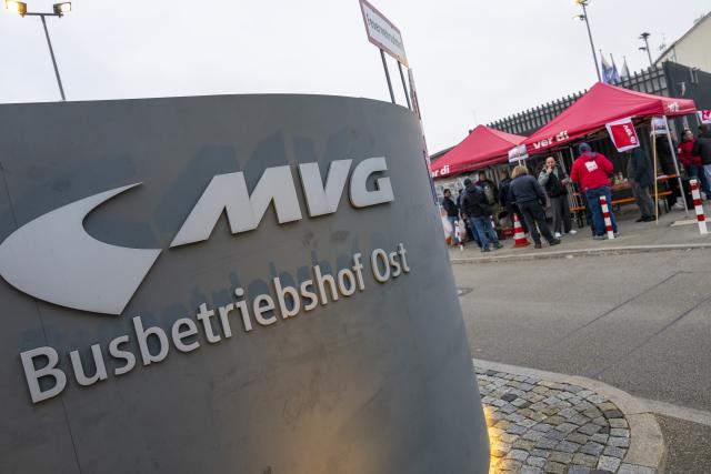 14 April 2026, Bavaria, Munich: Employees of the MVG East Depot stand behind a banner reading "Warning Strike Today" at the workshop gate on Truderinger Strasse during a warning strike affecting local public transportation. Photo: Peter Kneffel/dpa
