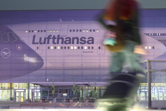 14 April 2026, Bavaria, Munich: People walk past a large image of a Lufthansa aircraft at Terminal 2 early in the morning on the second day of the pilots' strike. Photo: Karl-Josef Hildenbrand/dpa