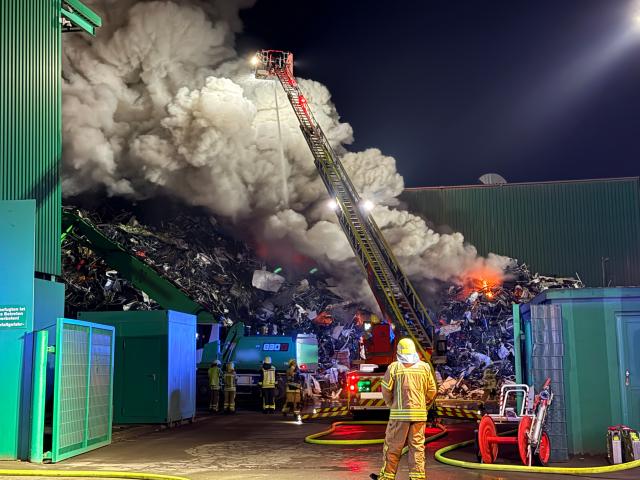 14 April 2026, North Rhine-Westphalia, Herne: Emergency responders extinguish a burning pile of scrap metal at a scrap yard in Herne after a fire triggered an early-morning response, with authorities warning residents about heavy smoke. Photo: Michael Weber/WTVnews/dpa - ACHTUNG: Schriftzüge wurde(n) aus rechtlichen Gründen gepixelt