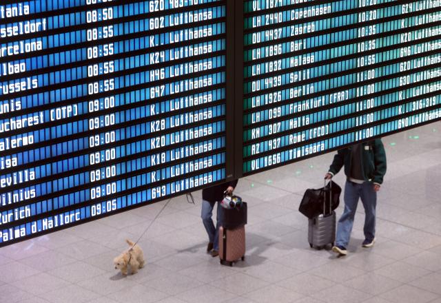 14 April 2026, Bavaria, Munich: People walk behind a departure board in Terminal 2 early in the morning on the second day of the Lufthansa pilots' strike. Photo: Karl-Josef Hildenbrand/dpa