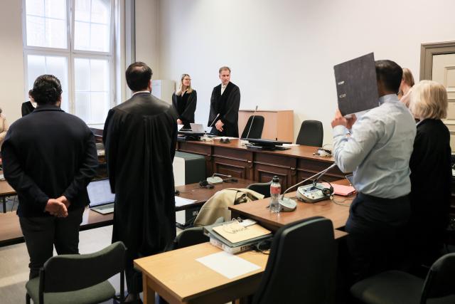 15 April 2026, Hamburg: Presiding judge at the regional court Thees Willemer (C), the two defendants (l and 2nd from right), their lawyers Mudgteba Laqmani (2nd from left) and Ina Franck (R) and other participants in the trial stand in the courtroom before the start of a trial for hostage-taking. A trial against a 25-year-old and a 27-year-old for hostage-taking began on Wednesday. Photo: Christian Charisius/dpa