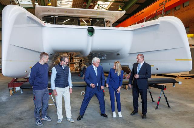 15 April 2026, Mecklenburg-Western Pomerania, Stralsund: German President Frank-Walter Steinmeier (C) looks for the right position for the photo opportunity in front of a catamaran sailing ship under construction during a visit to the Pioneer Yachts company on the Volkswerft shipyard site. As part of his "Local Time Germany" series of visits, the Federal President is moving his official residence to Stralsund until 16.04.2026. Photo: Jens Büttner/dpa