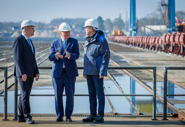 15 April 2026, Mecklenburg-Western Pomerania, Stralsund: German President Frank-Walter Steinmeier (M) stands with Peter Fürst (r), Head of the Office for Economic Development and City Marketing in Stralsund, and Alexander Badrow (l, CDU), Lord Mayor of the Hanseatic City of Stralsund, in front of the empty ship lift used to lift freighters out of and into the water during a visit to the Volkswerft industrial area. As part of his "Local Time Germany" series of visits, the Federal President is moving his official residence to Stralsund until 16.04.2026. Photo: Jens Büttner/dpa