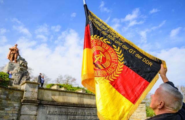 16 April 2026, Brandenburg, Seelow: A member of the Berlin Association for Preserving the Traditions of the National People's Army (NVA) and the Border Troops (GT) of the GDR participates in a commemorative event marking the 81st anniversary of the Battle of the Seelow Heights at the Seelow Heights Memorial and Museum, holding a GDR flag. The battle in April 1945 went down in history as the fiercest of World War II on German soil. Photo: Patrick Pleul/dpa