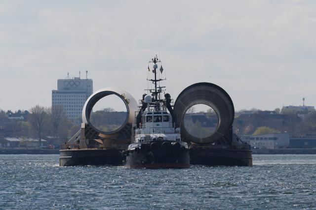 16 April 2026, Schleswig-Holstein, Kiel: Tugs are towing a barge carrying parts of an offshore wind turbine on the Kiel Fjord. Photo: Marcus Brandt/dpa