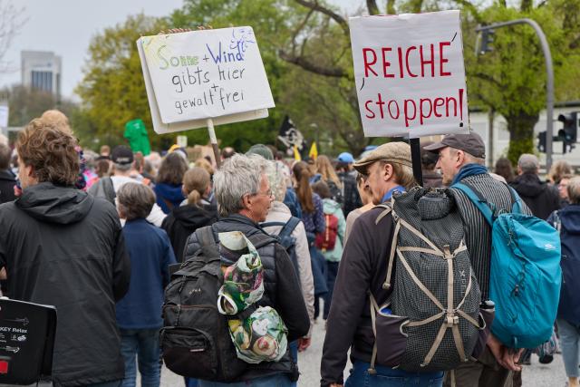 18 April 2026, Hamburg: Participants at a demonstration for the energy transition on Glockengießerwall hold banners reading "Sun+Wind is available here without violence" and "Stop the rich!". Campact, Deutsche Umwelthilfe, the Citizens' Energy Alliance, Greenpeace, WWF, Paritätische, Germanzero, Germanwatch and Fridays for Future called for protests across Germany. Photo: Georg Wendt/dpa