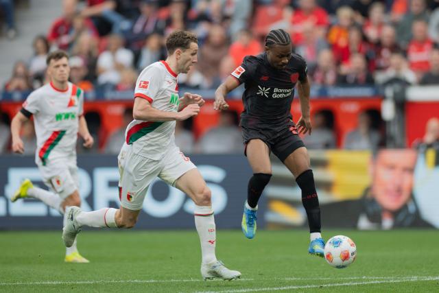 18 April 2026, North Rhine-Westphalia, Leverkusen: Bayer Leverkusen's Nathan Tella (R) and Augsburg's Arthur Chaves battle for the ball during the German Bundesliga soccer match between Bayer Leverkusen and FC Augsburg at BayArena. Photo: Rolf Vennenbernd/dpa - WICHTIGER HINWEIS: Gemäß den Vorgaben der DFL Deutsche Fußball Liga bzw. des DFB Deutscher Fußball-Bund ist es untersagt, in dem Stadion und/oder vom Spiel angefertigte Fotoaufnahmen in Form von Sequenzbildern und/oder videoähnlichen Fotostrecken zu verwerten bzw. verwerten zu lassen.