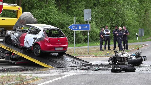 19 April 2026, North Rhine-Westphalia, Bruehl: A burned-out vehicle is loaded onto a tow truck while a motorcycle lies on the road in the southern part of Bruehl. One person was seriously injured in the traffic accident. Photo: -/dpa
