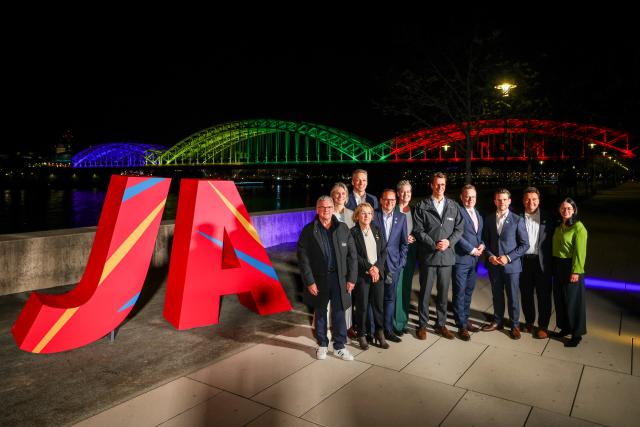 19 April 2026, North Rhine-Westphalia, Cologne: (L-R) Hendrik Wuest, Minister-President of North Rhine-Westphalia, and Torsten Burmester, Mayor of Cologne, stand in front of a large "Yes" sign and the Hohenzollern Bridge illuminated in the Olympic colours. Photo: Christoph Reichwein/dpa