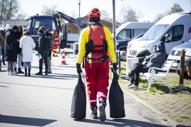 20 April 2026, Mecklenburg-Vorpommern, Wismar: A DLRG volunteer carries two bags to a boat as a humpback whale remains off the coast of Poel after briefly swimming away before stopping again despite attempts to guide it onward. Photo: Philip Dulian/dpa