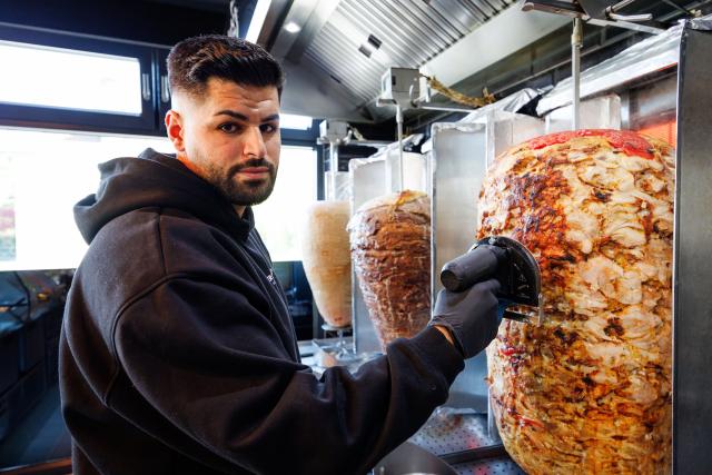 PRODUCTION - 21 April 2026, North Rhine-Westphalia, Bielefeld: Sergen Kolcu works on a rotisserie spit with chicken meat in a branch of "Krispy Kebab". The Bielefeld-based kebab chain operator Kolcu had the product "Krispy Kebab" legally protected years ago. Now the US fast food giant KFC is offering a product with the same name. Photo: Friso Gentsch/dpa