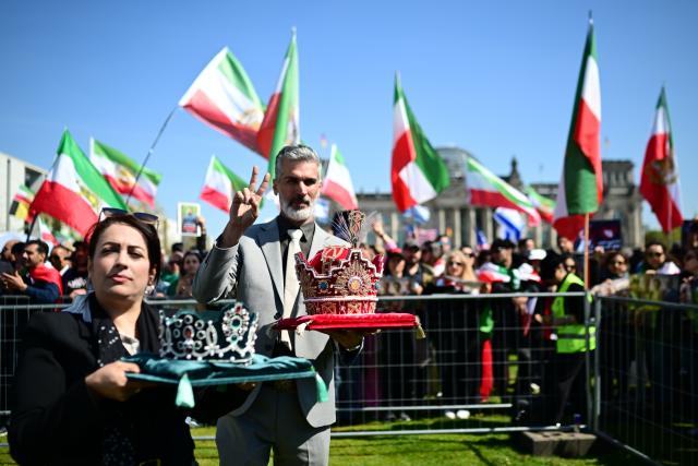23 April 2026, Berlin: Two people carry crowns past a demonstration titled 'Support for the Iranian Revolution on the Occasion of Crown Prince Reza Pahlavi's Visit to Berlin,' held in connection with the visit of the exiled son of Iran's former shah to the German capital. Photo: Sebastian Gollnow/dpa
