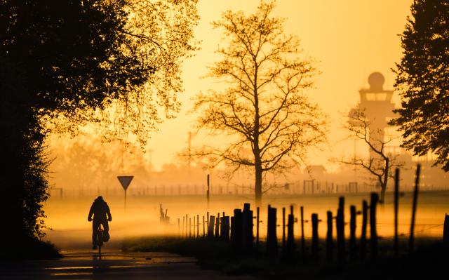 27 April 2026, Lower Saxony, Hanover: A man rides a bicycle at sunrise and in light fog near Hanover Airport. Photo: Julian Stratenschulte/dpa