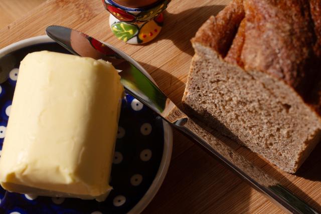 FILED - 10 March 2026, Berlin: A piece of butter lies on a plate next to a knife, and a sliced loaf of bread lies on a table next to it. Photo: Fernando Gutierrez-Juarez/dpa