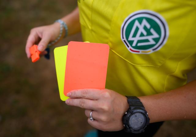 PRODUCTION - 24 July 2023, Sachsen, Kamenz: A referee stands on the field holding red and yellow cards. The German Football Federation (DFB) will decide after the World Cup whether or not to adopt a new rule under which players can be sent off if they cover their mouth when confronting an opponent. Photo: Robert Michael/dpa