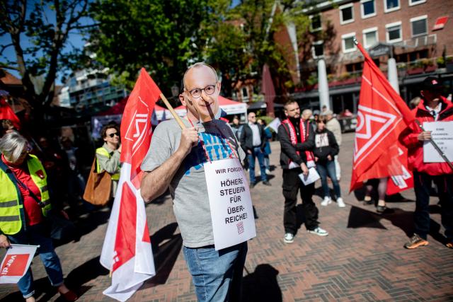 29 April 2026, Lower Saxony, Emden: Members of IG Metall wearing masks depicting German Chancellor Friedrich Merz, take part in a demonstration in the Stadtgarten in conjunction with the 14th National Maritime Conference (NMK). Photo: Hauke-Christian Dittrich/dpa