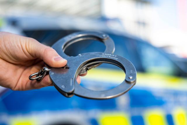 FILED - 28 September 2021, Nordrhein-Westfalen, Gütersloh: FILE PHOTO - A hand holds a pair of handcuffs in front of a police patrol car. Photo: David Inderlied/dpa