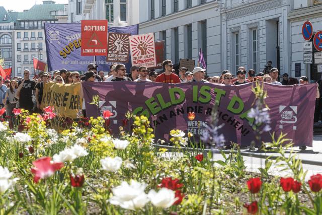 01 May 2026, Hamburg: People hold a banner reads "The money's there! Let's go after the rich!" at a demonstration calling for the redistribution of wealth. On May 1, several demonstrations and events are taking place across the country. Photo: Markus Scholz/dpa