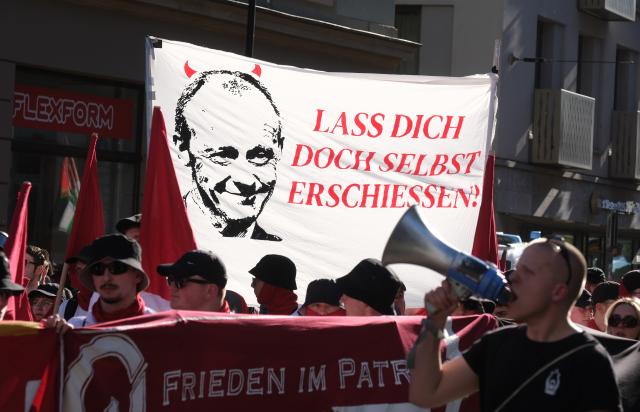 01 May 2026, Saxony, Leipzig: Participants in a left-wing demonstration carry a banner reading "Why don't you just get yourself shot?" and featuring a picture of Federal Chancellor Merz. On May 1, several demonstrations and events are taking place across the country. Photo: Sebastian Willnow/dpa