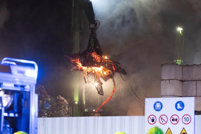 03 May 2026, North Rhine-Westphalia, Moenchengladbach: A crane lifts burning scrap metal on a company premises after a fire was reported around midnight. During a nighttime operation, firefighters were able to largely extinguish a pile of burning scrap metal at a waste disposal facility. Photo: Jan Ohmen/dpa