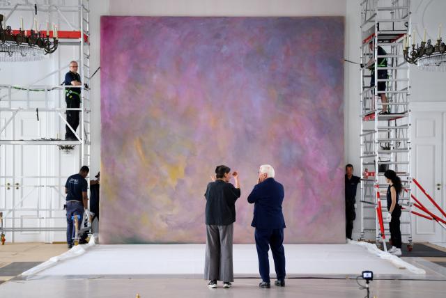 05 May 2026, Berlin: Employees of an art shipping company are hanging one of the two large works of art by the artist Gotthard Graubner (1930-2013), titled "Encounters," in the Great Hall of Bellevue Palace, in the presence of restorer Hana Streicher (center left) and Federal President Frank-Walter Steinmeier (center right). The palace is currently being prepared for a long-term renovation. The large color-space sculptures were created by Graubner in 1988 directly at Bellevue Palace at the request of Federal President von Weizsäcker. Photo: Bernd von Jutrczenka/dpa