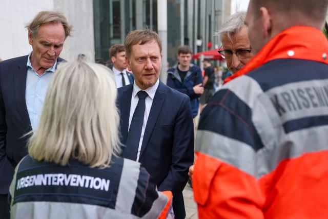 05 May 2026, Saxony, Leipzig: (L-R) Burkhard Jung, Lord Mayor of Leipzig, Michael Kretschmer, Minister President of Saxony, and Armin Schuster, Minister of the Interior of Saxony, speak  with staff from the crisis intervention team at the memorial site. The previous day, a 33-year-old German citizen had driven through the pedestrian zone in Grimmaische Strasse on a rampage. Two people were killed and three seriously injured. Photo: Jan Woitas/dpa