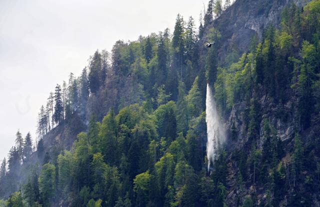 06 May 2026, Bavaria, Ruhpolding: A helicopter drops water to fight the large-scale wildfire on the 1,270-meter-high Sauruesselkopf in the Chiemgau Alps. Photo: Uwe Lein/dpa
