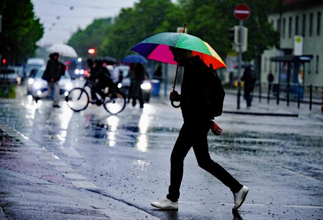 06 May 2026, Bavaria, Munich: A man with an umbrella walks across the intersection at Hackerbruecke. Photo: Malin Wunderlich/dpa