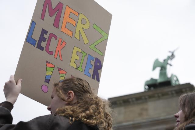08 May 2026, Berlin: A demonstrator holds up a sign with explicit language directed at German Chancellor Friedrich Merz as people gather in front of the Brandenburg Gate in Berlin to protest against the draft. Photo: Sven Kaeuler/dpa