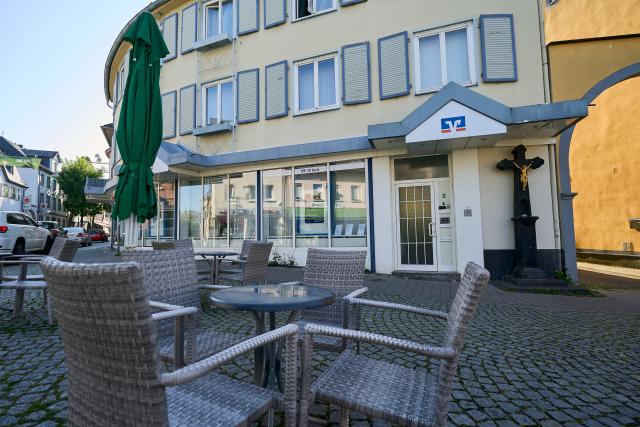09 May 2026, Rhineland-Palatinate, Sinzig: Tables and chairs from a cafe are set up outside the bank branch for guests. After a hours-long operation on Friday, police were able to free two people who had been held hostage inside the bank. The search for the perpetrator or perpetrators is still ongoing. Photo: Sascha Ditscher/dpa