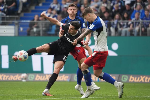 10 May 2026, Hamburg: Freiburg's Igor Matanovic (L) battles for the ball with Hamburger's Luka Vuskovic (R) and Nicolai Remberg during the German Bundesliga soccer match between Hamburger SV and SC Freiburg at Volksparkstadion. Photo: Marcus Brandt/dpa - IMPORTANT NOTE: In accordance with the regulations of the DFL German Football League and the DFB German Football Association, it is prohibited to utilize or have utilized photographs taken in the stadium and/or of the match in the form of sequential images and/or video-like photo series.