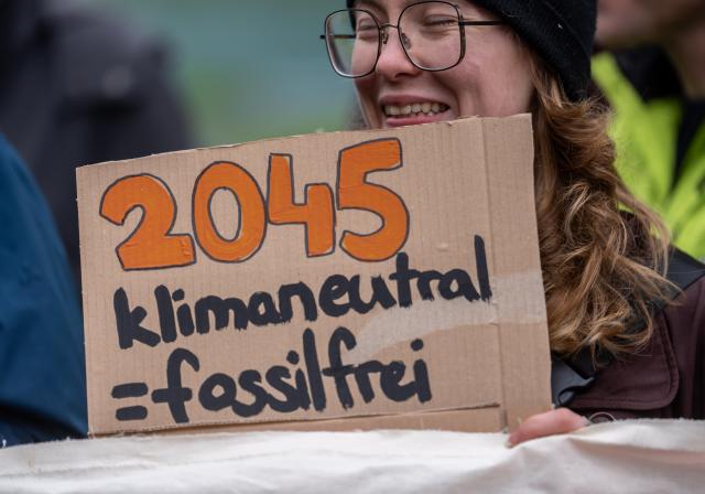 13 May 2026, Berlin: An activist holds a sign reading "2045 climate-neutral=fossil-free". Activists from various organizations demonstrate against the planned building modernization law in front of the German Chancellery. Photo: Michael Kappeler/dpa