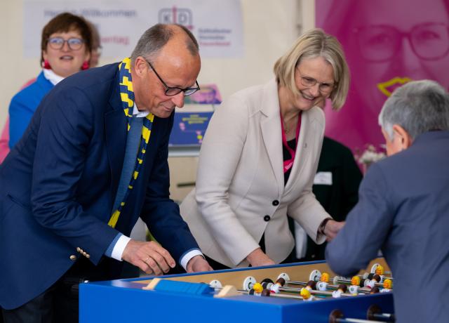 15 May 2026, Bavaria, Wuerzburg: German Chancellor Friedrich Merz plays table football at a stand during a tour of the Church Mile at the 104th German Catholic Day. Photo: Sven Hoppe/dpa - ATTENTION: For editorial use only and only with full reference to the above credit