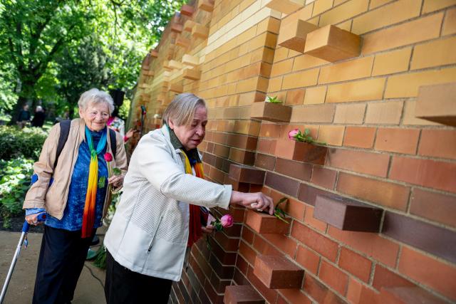 17 May 2026, Berlin: Two people lay roses at the Memorial Wall during the dedication of the new burial and memorial site for queer people, established by Schwulenberatung Berlin at St. Matthaeus Churchyard. Photo: Fabian Sommer/dpa