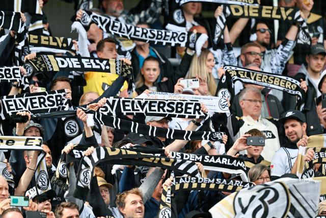 17 May 2026, Spiesen-Elversberg: Elversberg fans hold up their scarves during the German 2nd Bundesliga soccer match between SV Elversberg and Preussen Muenster at the Ursapharm-Arena an der Kaiserlinde. Photo: Uwe Anspach/dpa - IMPORTANT NOTE: In accordance with the regulations of the DFL German Football League and the DFB German Football Association, it is prohibited to utilize or have utilized photographs taken in the stadium and/or of the match in the form of sequential images and/or video-like photo series.