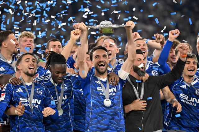 17 May 2026, North Rhine-Westphalia, Gelsenkirchen: Schalke's Kenan Karaman celebrates holds up the 2nd Bundesliga trophy as he celebrates with team following the German 2nd Budnesliga soccer match between FC Schalke 04 and Eintracht Braunschweig at the Veltins Arena. Photo: Bernd Thissen/dpa - IMPORTANT NOTICE: DFL and DFB regulations prohibit any use of photographs as image sequences and/or quasi-video.
