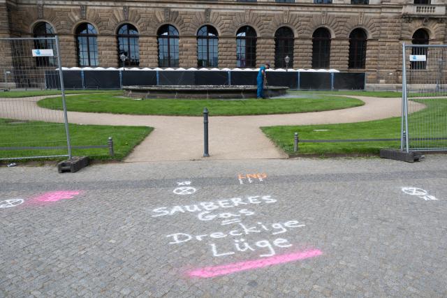 21 May 2026, Hamburg: "Clean Gas = Dirty Lie" is spray-painted on the pavement in front of an empty fountain basin on Theaterplatz outside the Semperoper in Dresden. Activists from the Extinction Rebellion environmental movement dyed fountains green across numerous German cities to protest against the federal government's liquefied natural gas (LNG) and economic policies. Photo: Bodo Marks/dpa