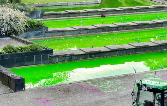 21 May 2026, Hamburg: Fountain water tinted green by climate activists flows in the Planten un Blomen park in Hamburg, next to the spray-painted slogan "Unfortunately not green". Activists from the Extinction Rebellion (XR) group claimed responsibility for the stunt, stating they used a harmless organic dye called uranine to protest against Germany's liquefied natural gas (LNG) policies. Photo: Bodo Marks/dpa