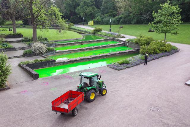 21 May 2026, Hamburg: Fountain water tinted green by climate activists flows in the Planten un Blomen park in Hamburg, next to the spray-painted slogan "Unfortunately not green". Activists from the Extinction Rebellion (XR) group claimed responsibility for the stunt, stating they used a harmless organic dye called uranine to protest against Germany's liquefied natural gas (LNG) policies. Photo: Bodo Marks/dpa