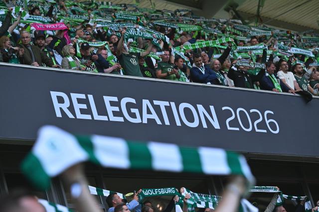 21 May 2026, Lower Saxony, Wolfsburg: Spectators hold up scarves and stand in front of a banner reading "RELEGATION 2026" during the German Bundesliga relegation playoff soccer match between VfL Wolfsburg and SC Paderborn 07 at Volkswagen Arena. Photo: Swen Pförtner/dpa - WICHTIGER HINWEIS: Gemäß den Vorgaben der DFL Deutsche Fußball Liga bzw. des DFB Deutscher Fußball-Bund ist es untersagt, in dem Stadion und/oder vom Spiel angefertigte Fotoaufnahmen in Form von Sequenzbildern und/oder videoähnlichen Fotostrecken zu verwerten bzw. verwerten zu lassen.