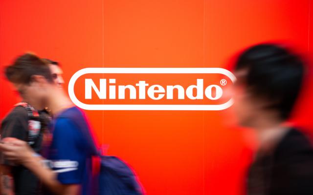 FILED - 13 August 2018, North Rhine-Westphalia, Cologne: FILE PHOTO - Visitors of Gamescom walk past the Nintendo logo. Photo: Christophe Gateau/dpa