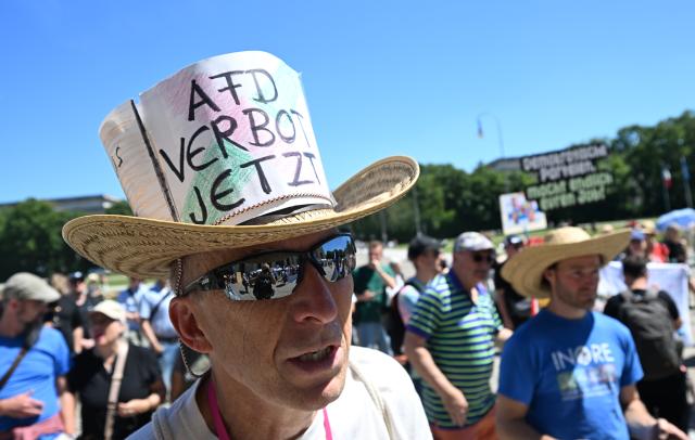 23 May 2026, Bavaria, Munich: A protester wearing a hat emblazoned with the words 'Ban the AfD Now' stands on Koenigsplatz square during the nationwide day of action titled 'Defend Human Dignity - Ban the AfD Now!'. Photo: Felix Hörhager/dpa