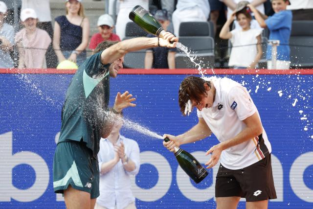 23 May 2026, Hamburg: American tennis player Tommy Paul (L) and winner Peru's Ignacio Buse (R) are doused with champagne during the award ceremony after the men's singles final of the Hamburg Open tennis tournament. Photo: Georg Wendt/dpa