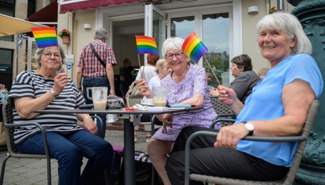 30 May 2026, Hesse, Wiesbaden: Three participants wave a rainbow flag during a break at an ice cream parlor during the Christopher Street Day event in Wiesbaden. According to the organizers, the group "Warmes Wiesbaden" plans to use Saturday's Pride event to stand up for an open society and against discrimination and anti-queer sentiment. Photo: Hannes P. Albert/dpa